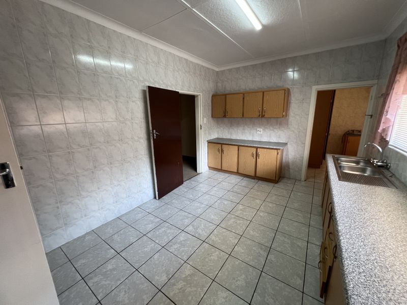 A functional, empty kitchen featuring tiled walls, tiled flooring, built-in wooden cabinetry, and a stainless steel sink.