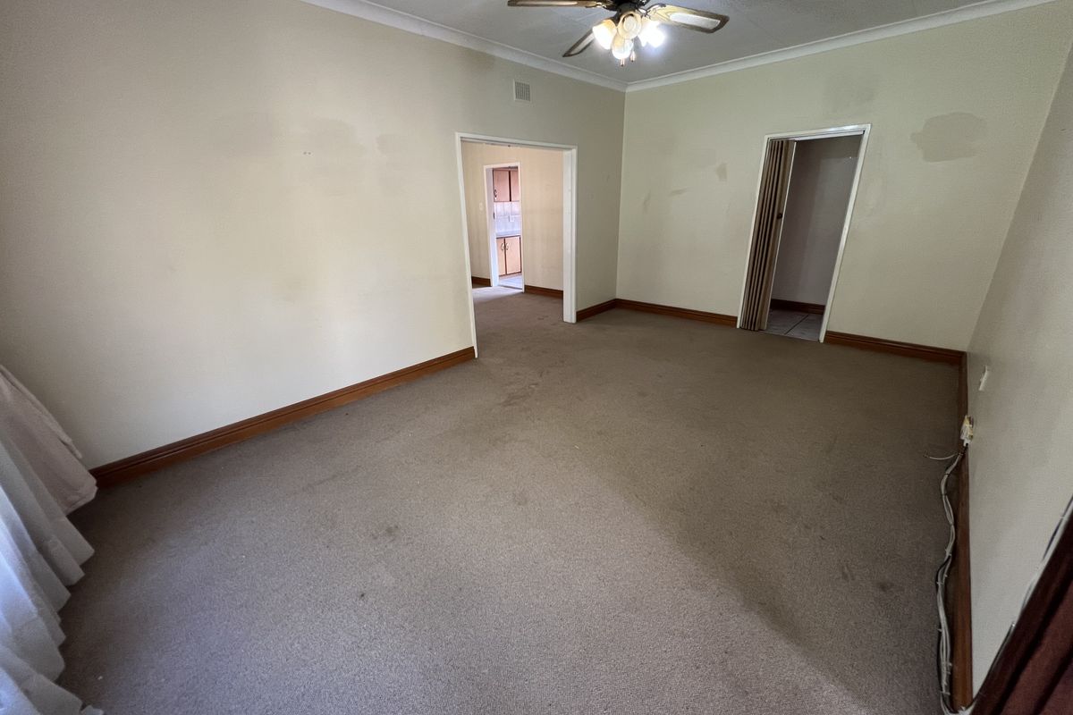 An empty living room featuring carpet flooring, a ceiling fan, and access to adjacent rooms through internal doorways.