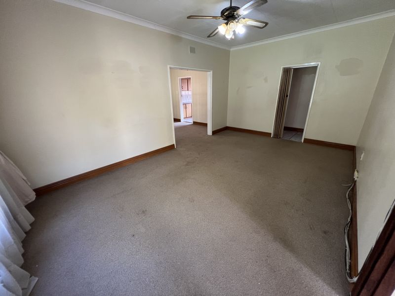 An empty living room featuring carpet flooring, a ceiling fan, and access to adjacent rooms through internal doorways.