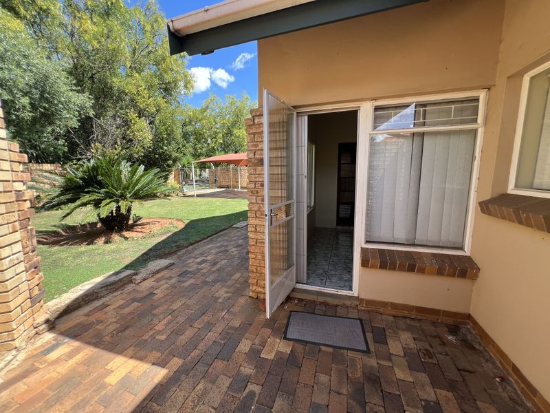 A covered brick-paved patio area providing direct access to the garden, featuring a security gate and brick structural elements.
