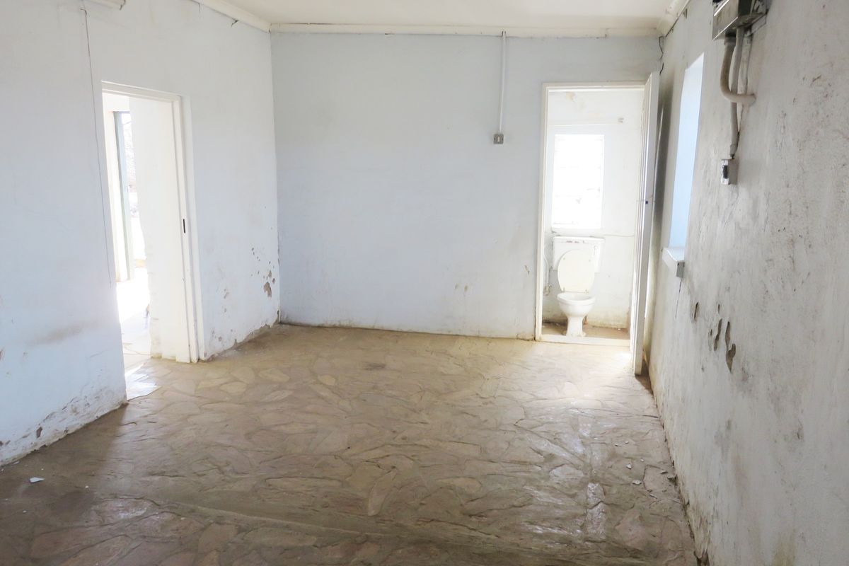 An empty, dated living area featuring stone flooring and visible wall damage, with an adjacent small room containing a toilet.