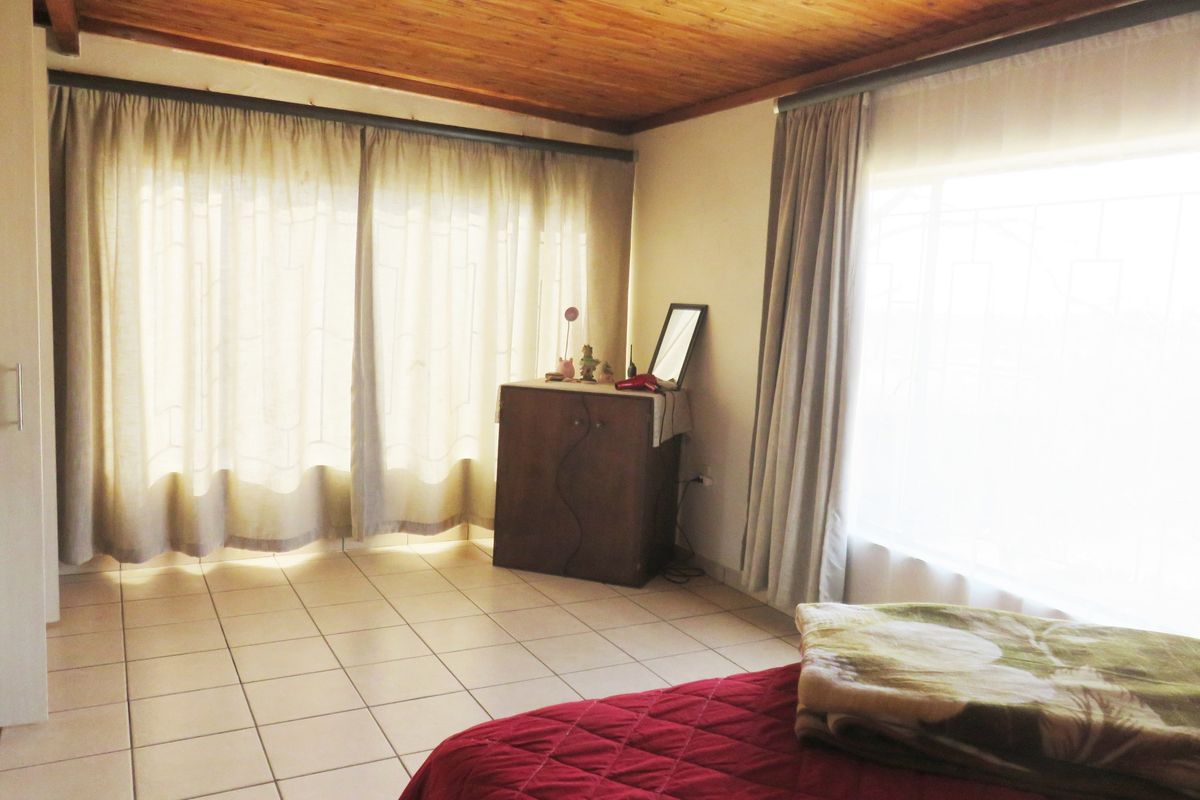 A bedroom featuring tiled flooring and a warm exposed timber ceiling, offering a functional space with natural light.