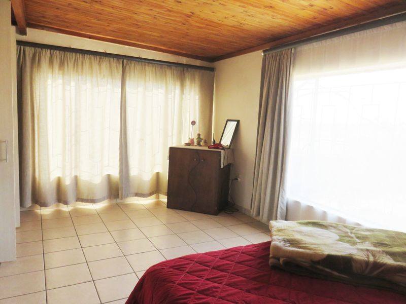 A bedroom featuring tiled flooring and a warm exposed timber ceiling, offering a functional space with natural light.