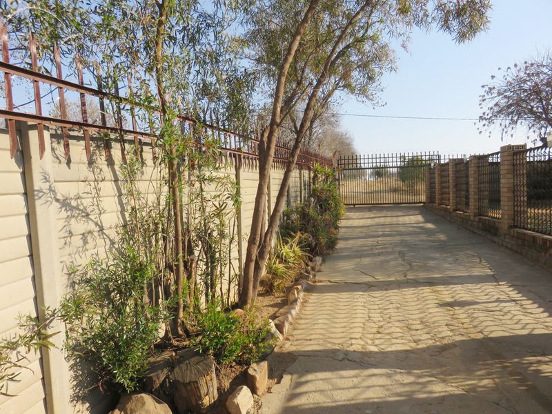 A driveway approach featuring a precast concrete boundary wall with security spikes, leading to a metal entrance gate.