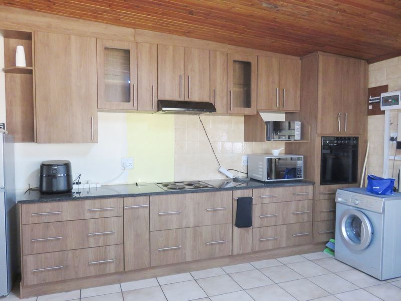 A functional kitchen featuring wood-finish cabinetry, granite countertops, built-in oven, electric hob, and tiled flooring with a timber-clad ceiling.