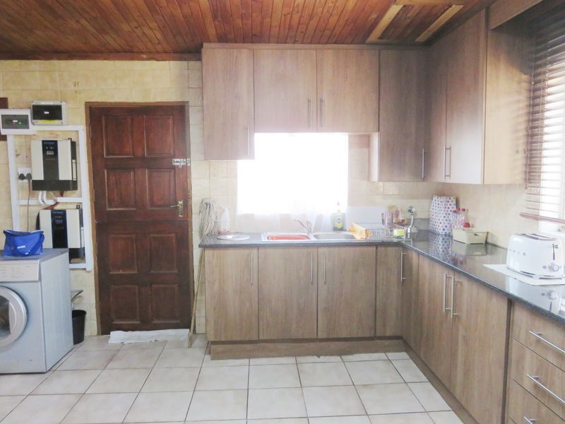 Functional kitchen featuring wood-look cabinetry, granite countertops, double basin sink, and tiled flooring, complemented by a timber-paneled ceiling.
