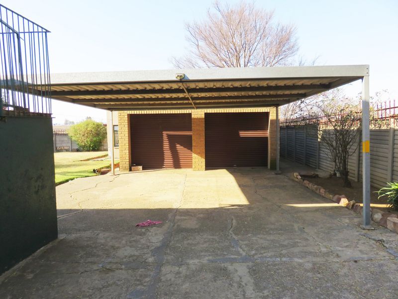 A double garage with an attached metal carport structure and a concrete driveway, set within a fenced residential property.