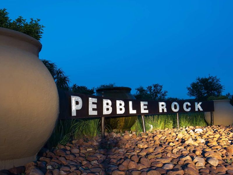 A well-maintained entrance sign for Pebble Rock estate, featuring professional landscape lighting and decorative stone elements at dusk.