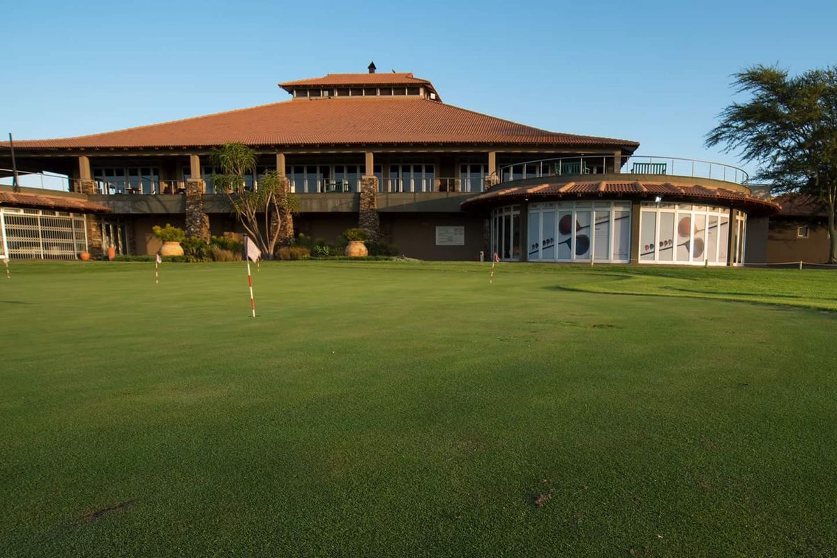 A well-maintained clubhouse exterior featuring a tiled roof, stone accents, and a balcony overlooking a manicured golf putting green.