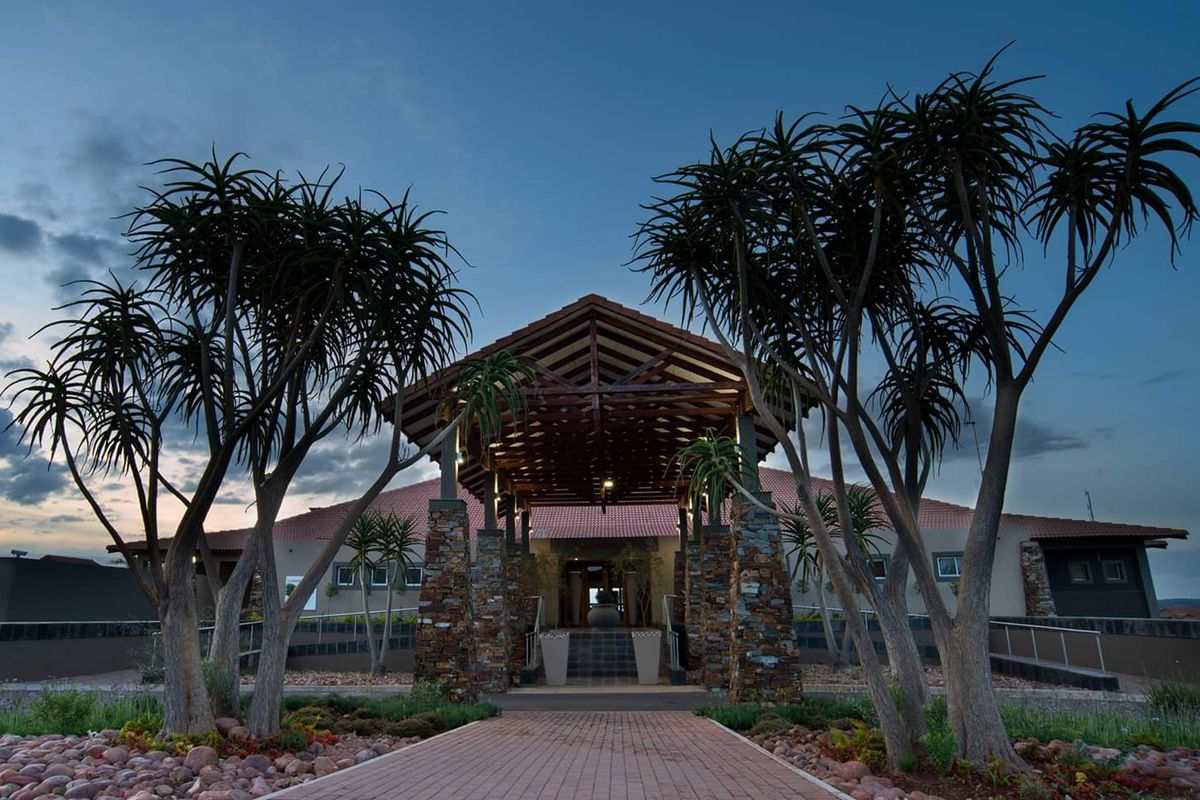 A striking front entrance featuring a timber-truss porte-cochere, stone-clad pillars, and a well-maintained paved walkway leading to the main building.