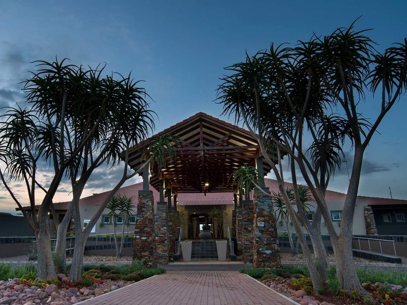A striking front entrance featuring a timber-truss porte-cochere, stone-clad pillars, and a well-maintained paved walkway leading to the main building.