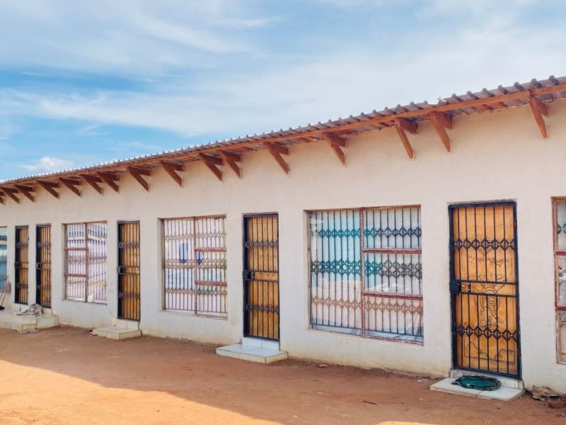 A row of residential units featuring corrugated metal roofing, exposed timber rafters, and security-gated entrances with protective window bars.