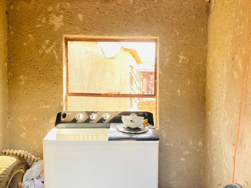 A small, unfinished utility or laundry space featuring raw plaster walls and a metal window frame, requiring significant renovation and finishing.