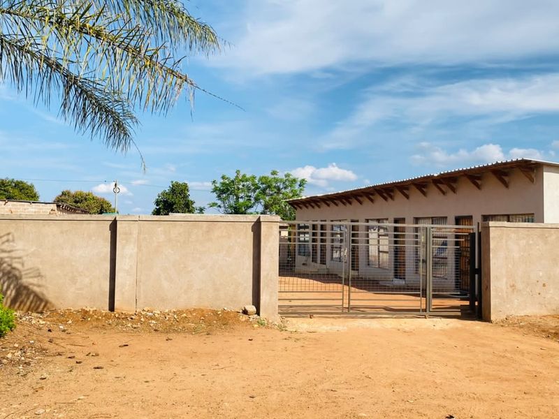 Front view of a single-story property featuring a perimeter wall, metal gate, and a corrugated metal roof with security bars on the windows.