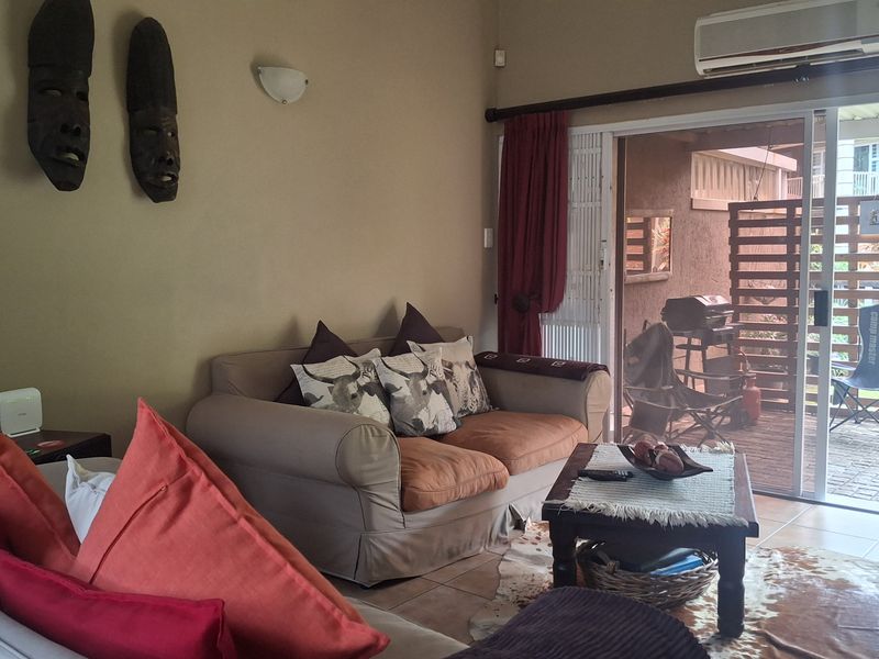 A comfortable living room featuring tiled flooring, a wall-mounted air conditioning unit, and large sliding glass doors providing access to an outdoor patio area.