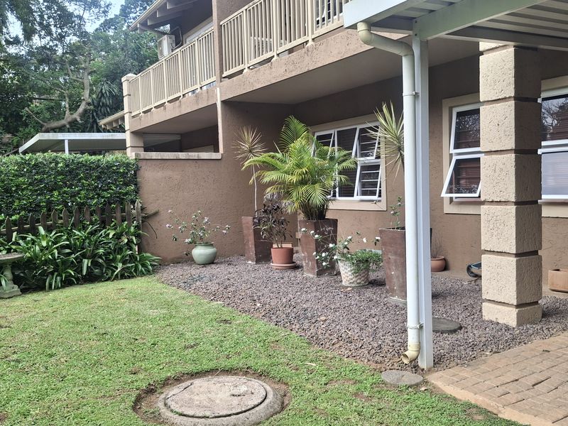 Rear exterior view of the townhouse featuring a covered patio, gravel garden area, lawn, and an upper-level balcony with railings.