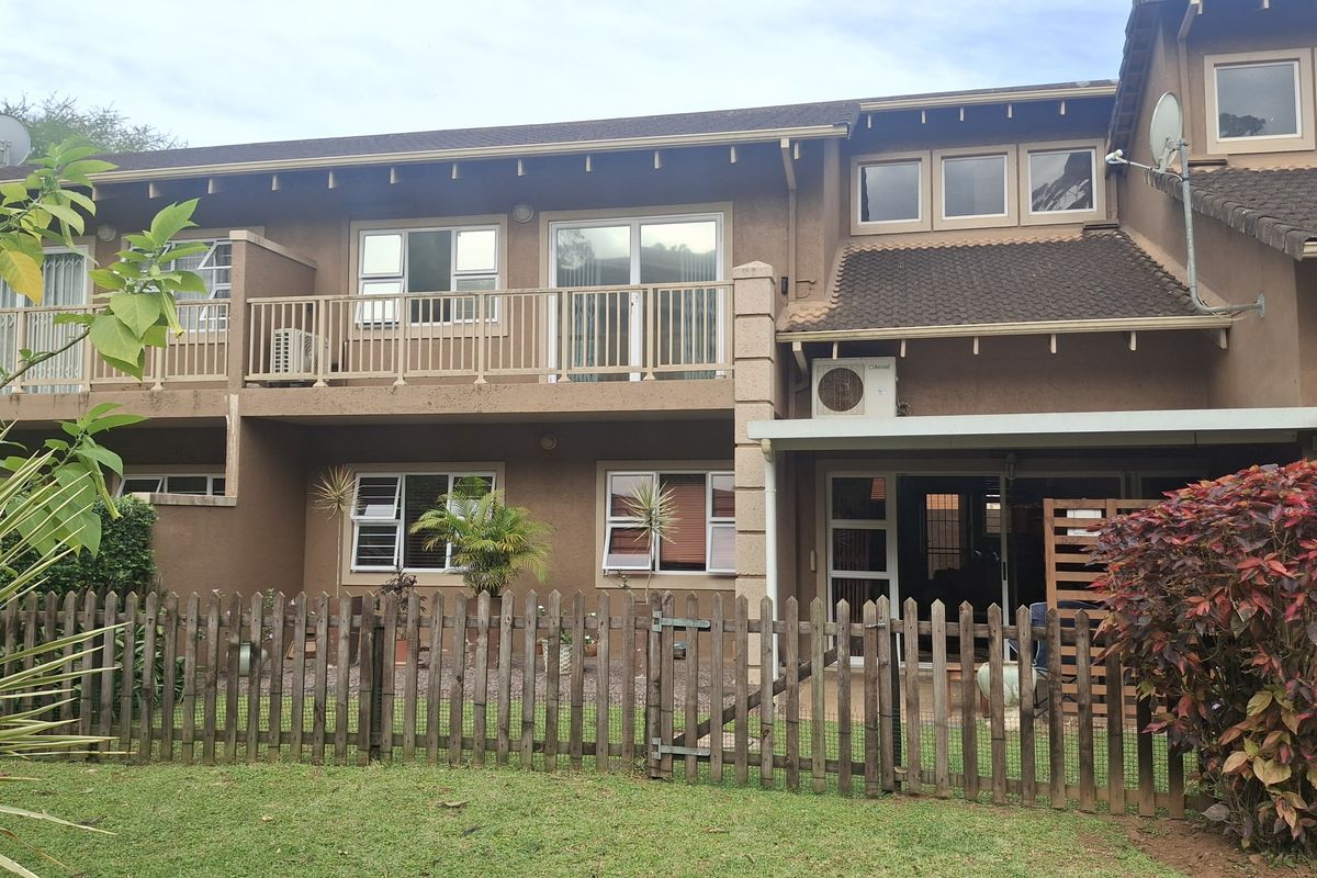 Rear elevation of a two-story townhouse featuring a balcony, sliding glass doors, and a private fenced garden area.