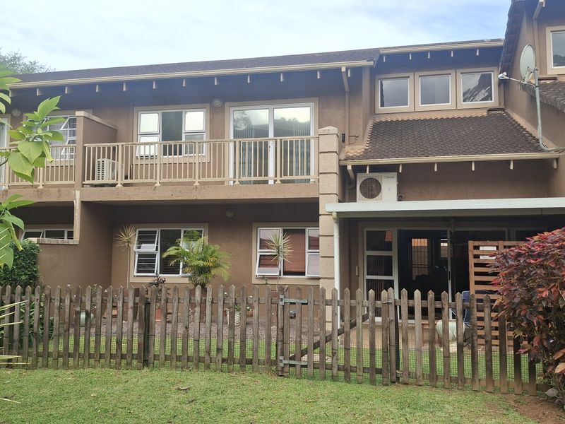Rear elevation of a two-story townhouse featuring a balcony, sliding glass doors, and a private fenced garden area.