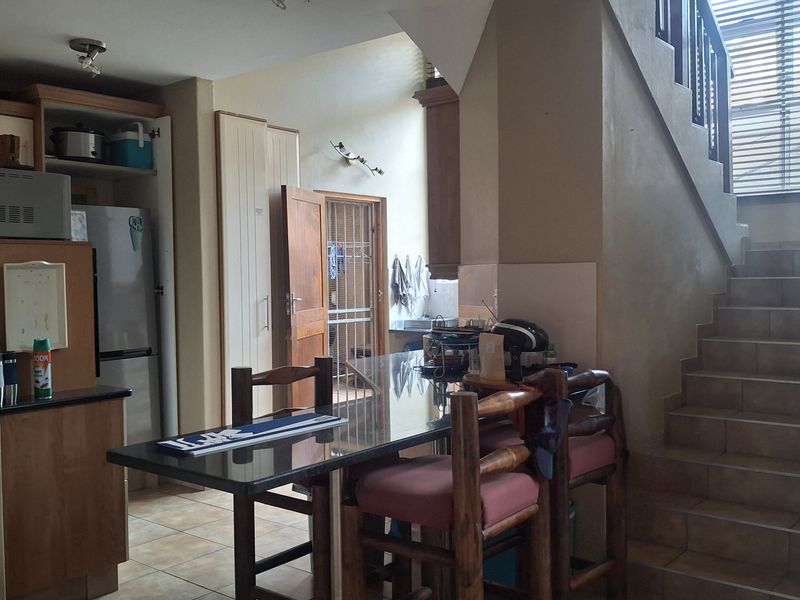 Open plan kitchen and dining area featuring built-in cabinetry, granite countertops, tiled flooring, and an adjacent staircase leading to the upper level.