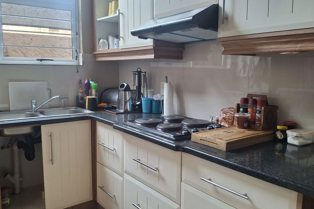 A functional kitchen featuring granite countertops, built-in cabinetry, an electric hob with extractor fan, and a stainless steel sink under a window.