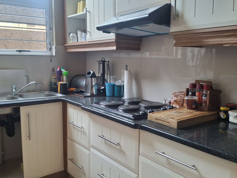 A functional kitchen featuring granite countertops, built-in cabinetry, an electric hob with extractor fan, and a stainless steel sink under a window.