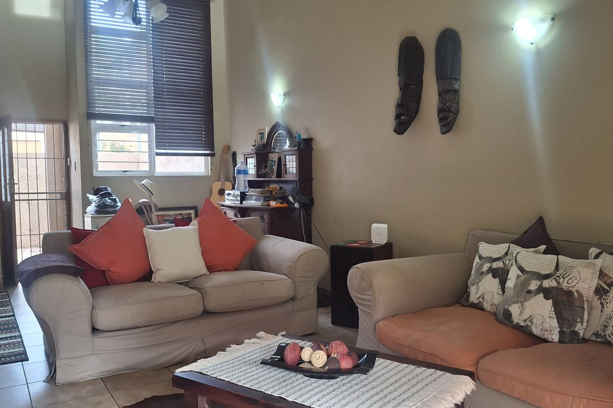 A living room area featuring tiled flooring, a staircase, and natural light through venetian blinds, offering a functional space for relaxation.