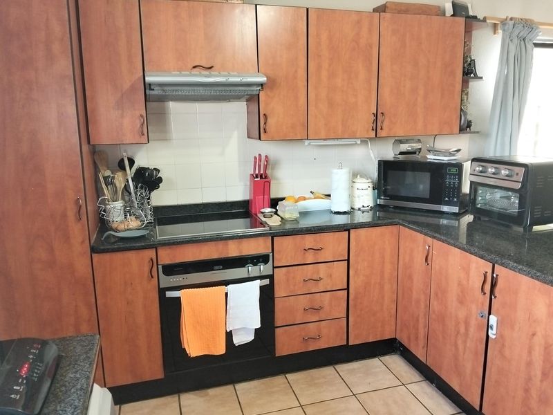 A functional kitchen featuring wood-finish cabinetry, granite countertops, a built-in oven with hob, and an extractor fan, complemented by tiled flooring and backsplash.
