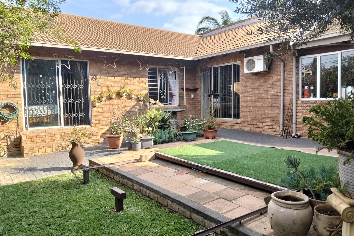 Rear exterior view of a brick duet property featuring a paved patio area, artificial grass section, and sliding door access to the interior.