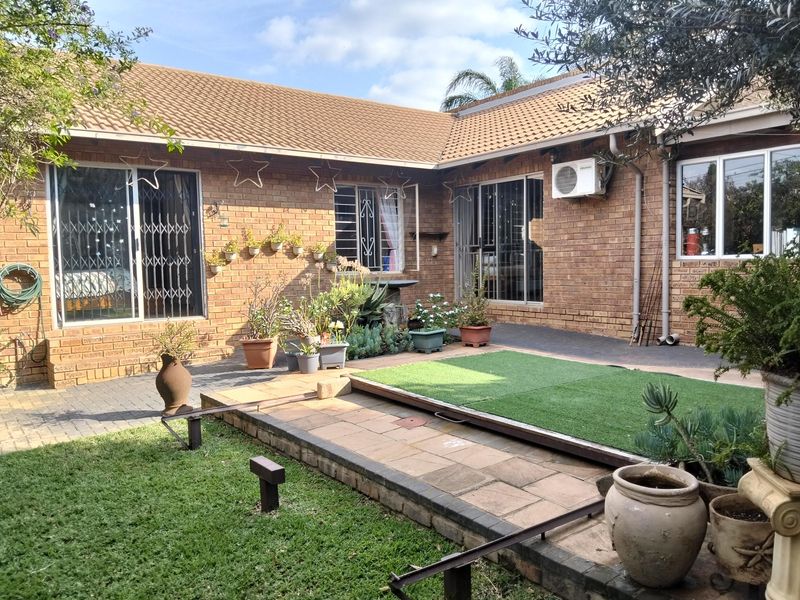 Rear exterior view of a brick duet property featuring a paved patio area, artificial grass section, and sliding door access to the interior.