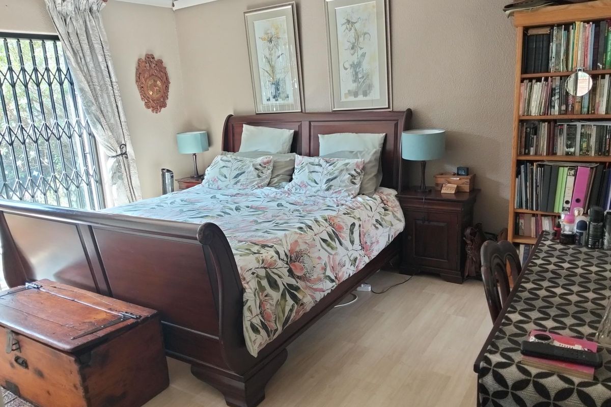 A comfortable bedroom featuring light-toned laminate flooring, a ceiling fan, and a security gate leading to the exterior.