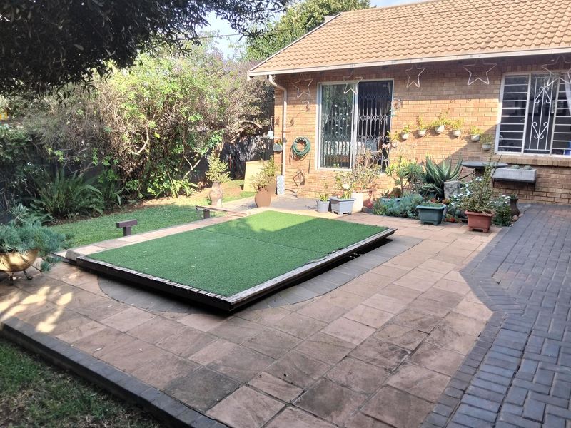 Rear exterior view featuring a brick facade, paved patio area, and a raised artificial grass platform, providing a functional outdoor space.