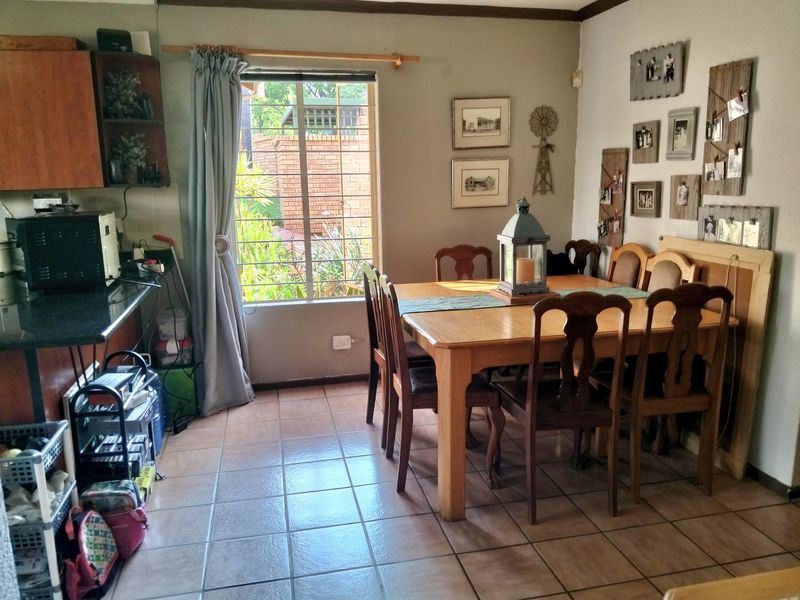 Open plan dining area featuring tiled flooring and a window with security bars, adjacent to a kitchen workspace.