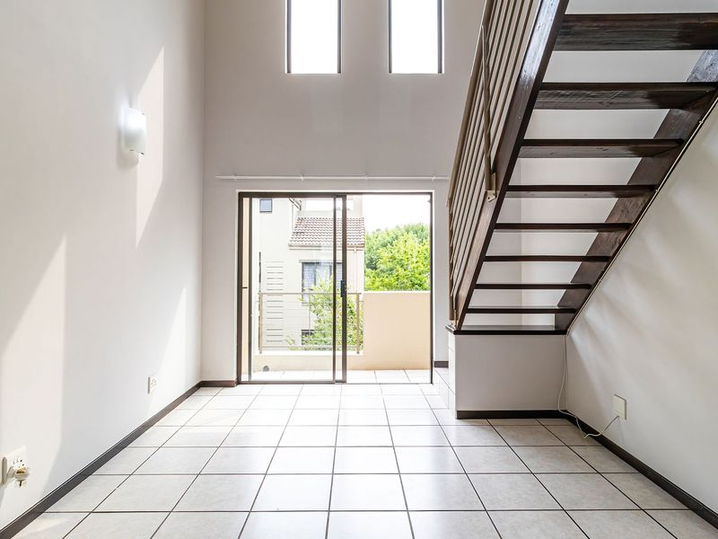 Bright, double-volume living area featuring tiled flooring, a modern staircase, and sliding glass doors leading to an outdoor balcony.