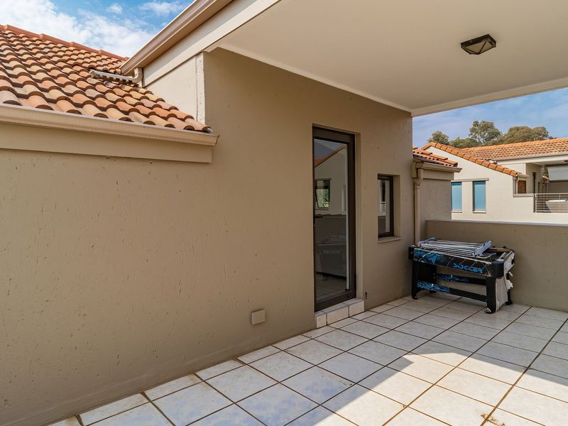 A covered balcony featuring tiled flooring, a glass door entrance, and terracotta roof detailing, providing a functional outdoor space.