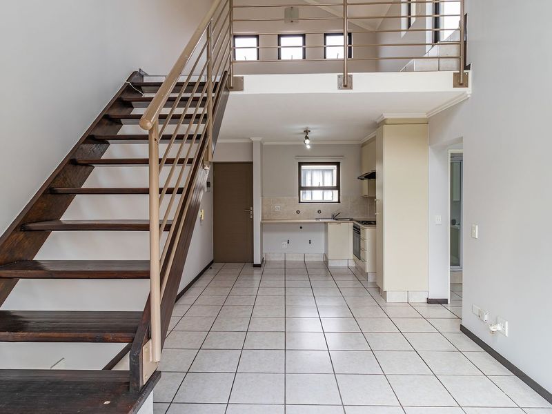 Open-plan living area featuring a mezzanine level, tiled flooring, and a functional kitchen with built-in cabinetry and appliances.