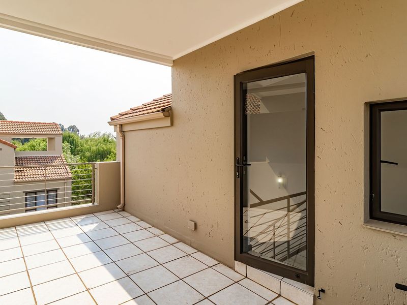 A clean, covered balcony featuring tiled flooring, a metal balustrade, and aluminium-framed glass access points, offering a pleasant outdoor space.