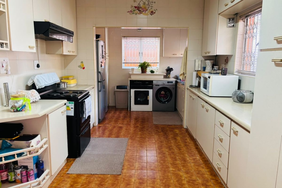 A functional kitchen featuring built-in cabinetry, laminate countertops, and integrated appliances, with a connected laundry area and tiled finishes throughout.