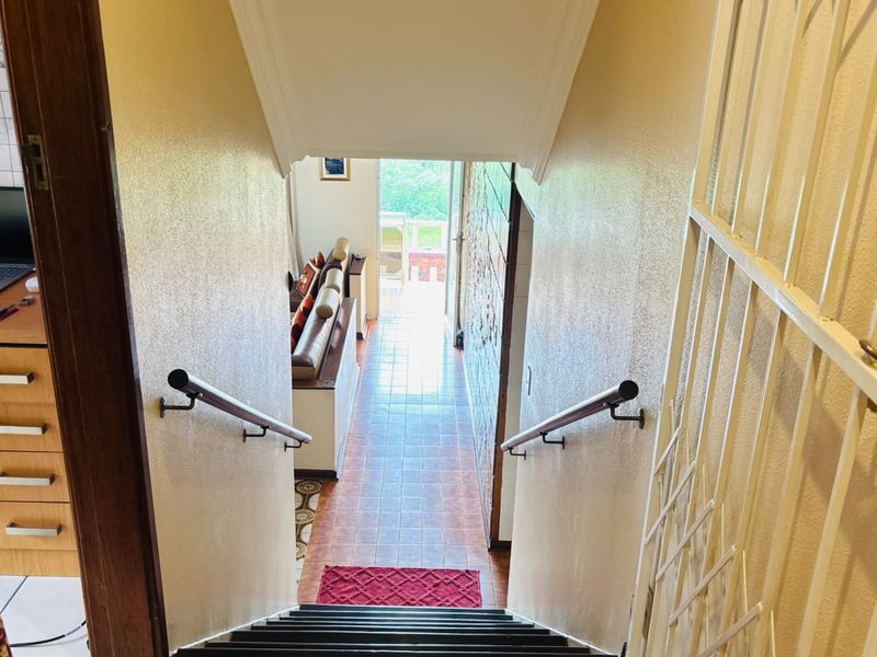 A view looking down a staircase into a tiled hallway leading towards an exterior doorway, featuring metal handrails and a security gate.
