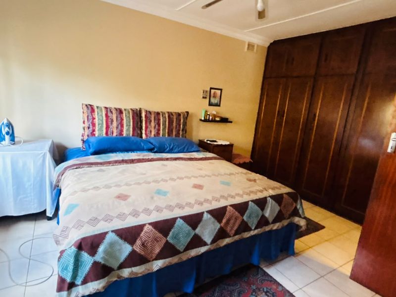 A bedroom featuring built-in wooden cupboards, tiled flooring, and a ceiling fan.
