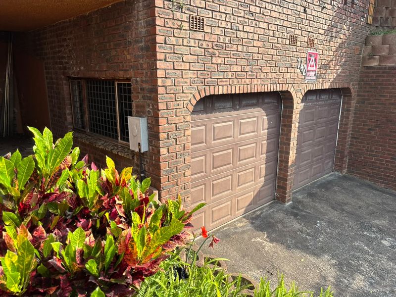 A double garage with brick facade and secure garage doors, featuring integrated security bars on the side window.