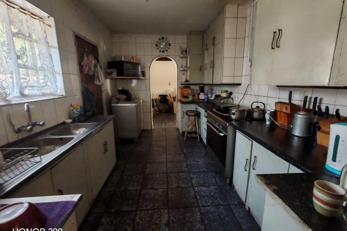 A functional kitchen featuring tiled flooring, built-in cabinetry, a double basin sink, and a freestanding oven, offering potential for modernization.