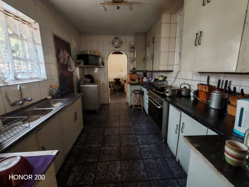 A functional kitchen featuring tiled flooring, built-in cabinetry, a double basin sink, and a freestanding oven, offering potential for modernization.