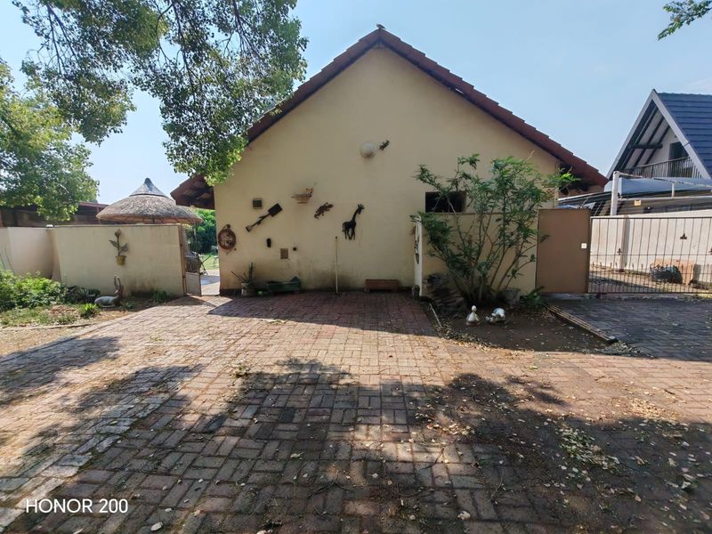Rear exterior view of the property featuring a paved driveway, boundary wall, and tiled roof structure.