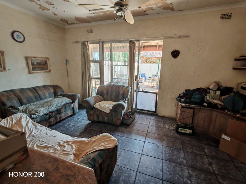 Living room featuring tiled flooring, a ceiling fan, and sliding glass doors leading to the exterior. The space requires significant cosmetic renovation and ceiling repairs.