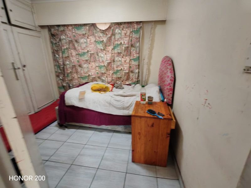 A bedroom featuring built-in cupboards and tiled flooring, currently requiring cosmetic updates to the wall finishes.