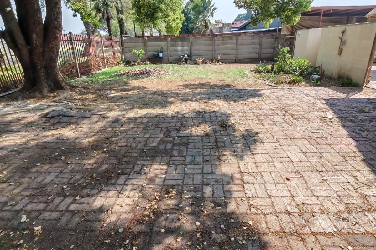 A spacious rear garden featuring a large paved patio area, mature trees, and perimeter fencing, offering potential for landscaping and outdoor entertainment development.
