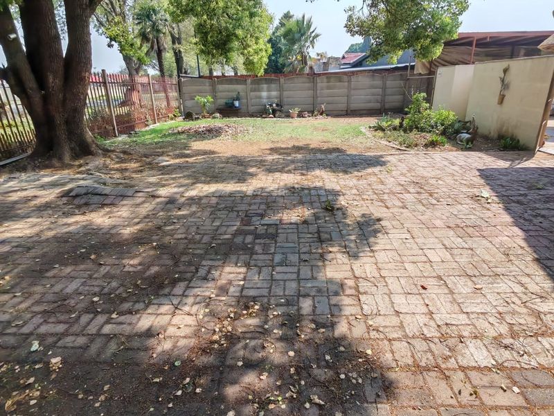 A spacious rear garden featuring a large paved patio area, mature trees, and perimeter fencing, offering potential for landscaping and outdoor entertainment development.