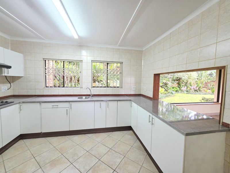 A functional kitchen featuring white cabinetry, stone countertops, tiled walls and floors, and a large window overlooking the garden.