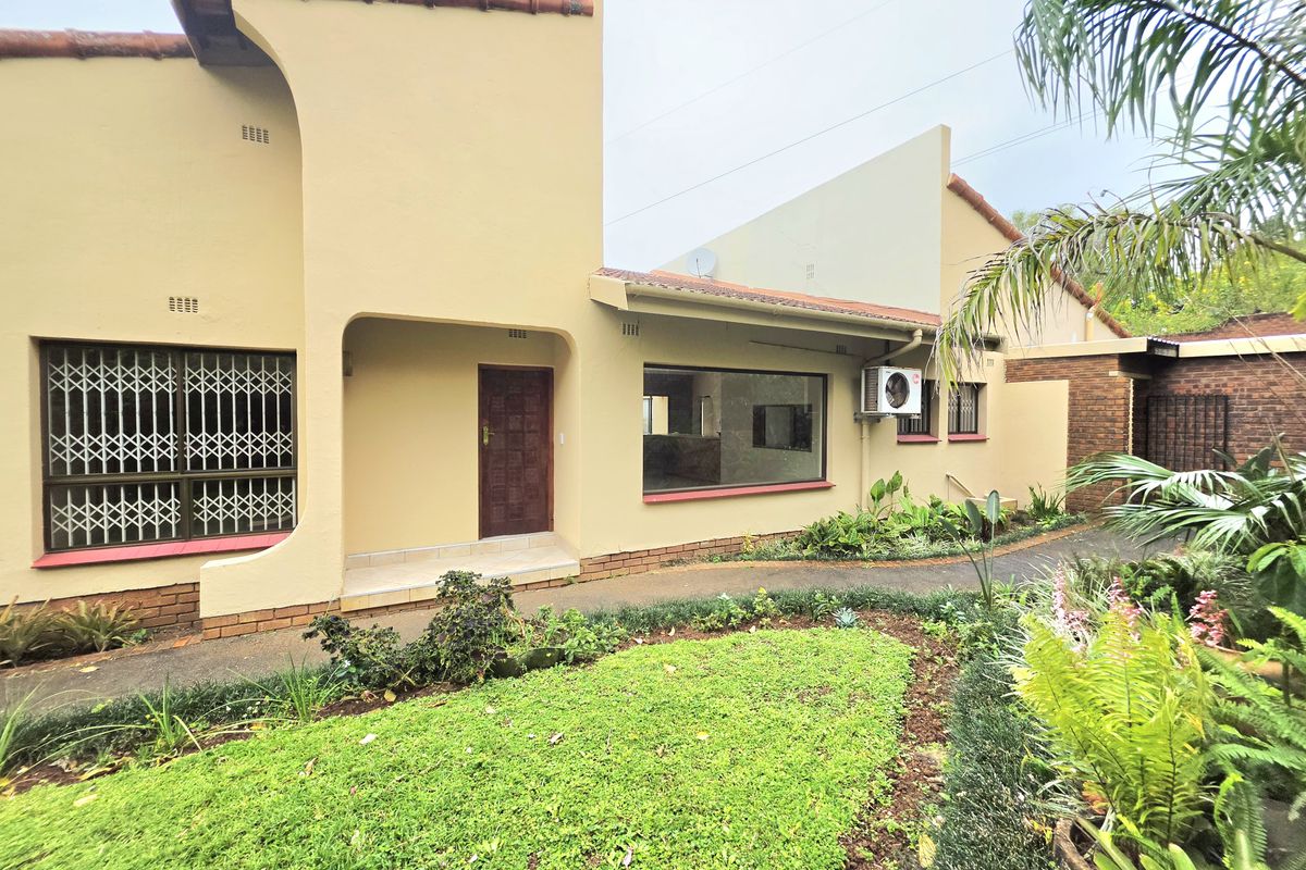 Rear exterior view of the house featuring a paved walkway, landscaped garden, security gates, and an installed air conditioning unit.