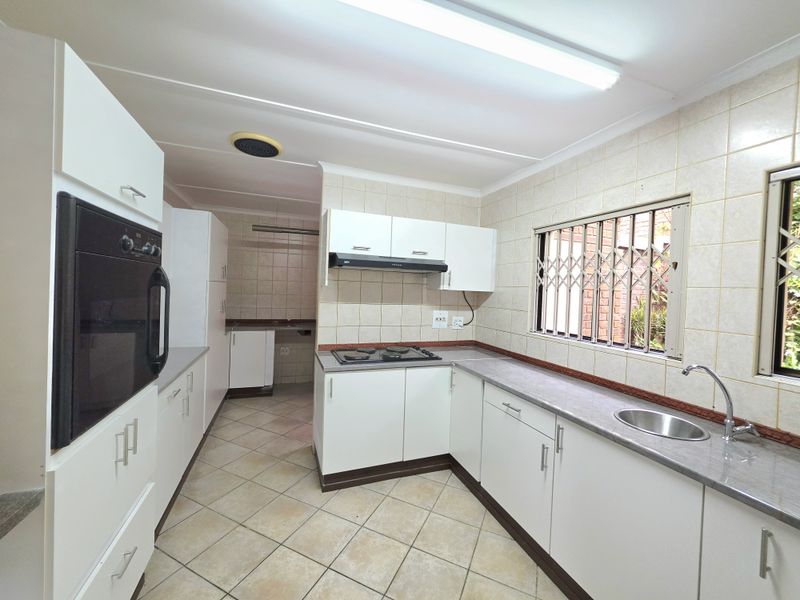A functional kitchen featuring built-in cabinetry, a hob, an oven, and a stainless steel sink with tiled finishes throughout.